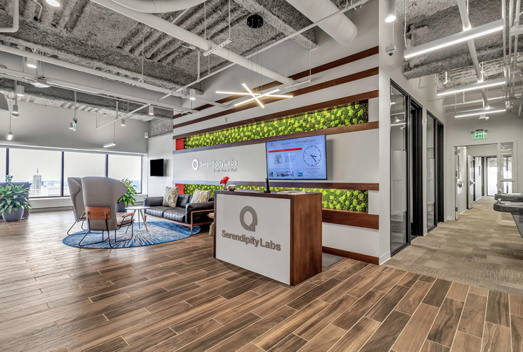 Main lobby area with open Coworking seating, front desk, views of the city, and main hallway with built-in water fountain.