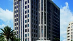 A tall, modern office building with many windows—home to Serendipity Labs coworking offices and meeting rooms—is surrounded by palm trees and greenery, standing against a blue sky dotted with scattered clouds.