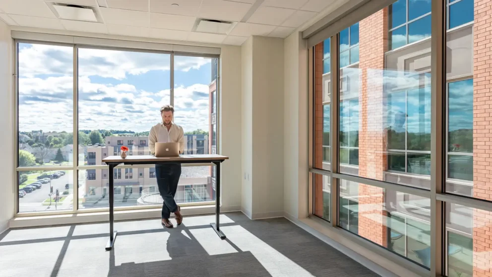 A man working in a private office with a large window view behind him. West Madison Private Office & Coworking Space