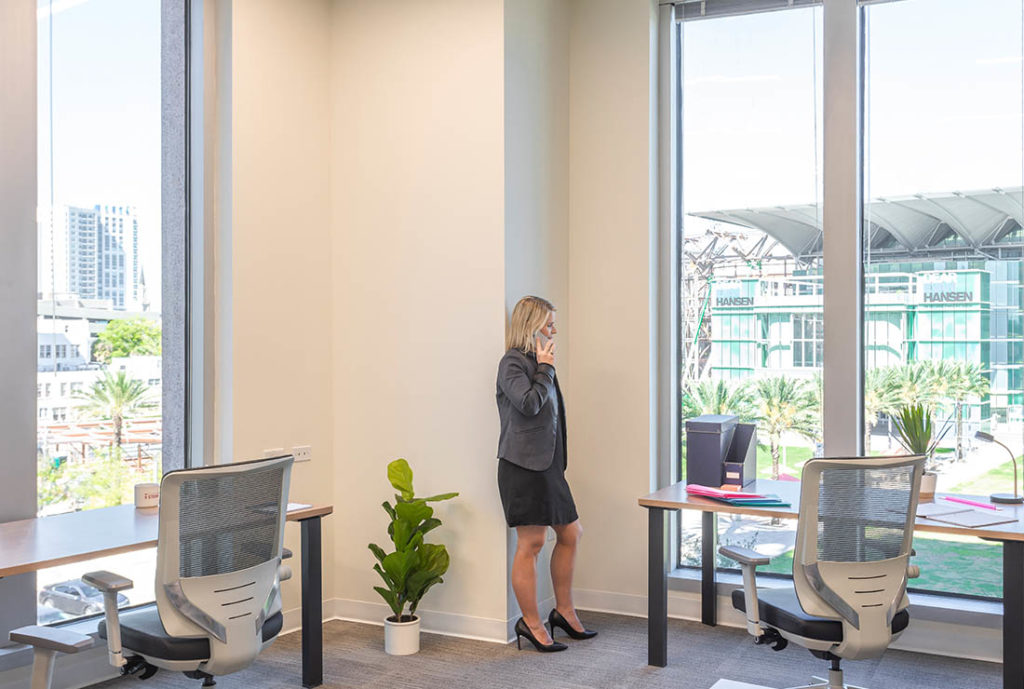 Woman on phone in a Private 2 person office, looking at the downtown through her window.