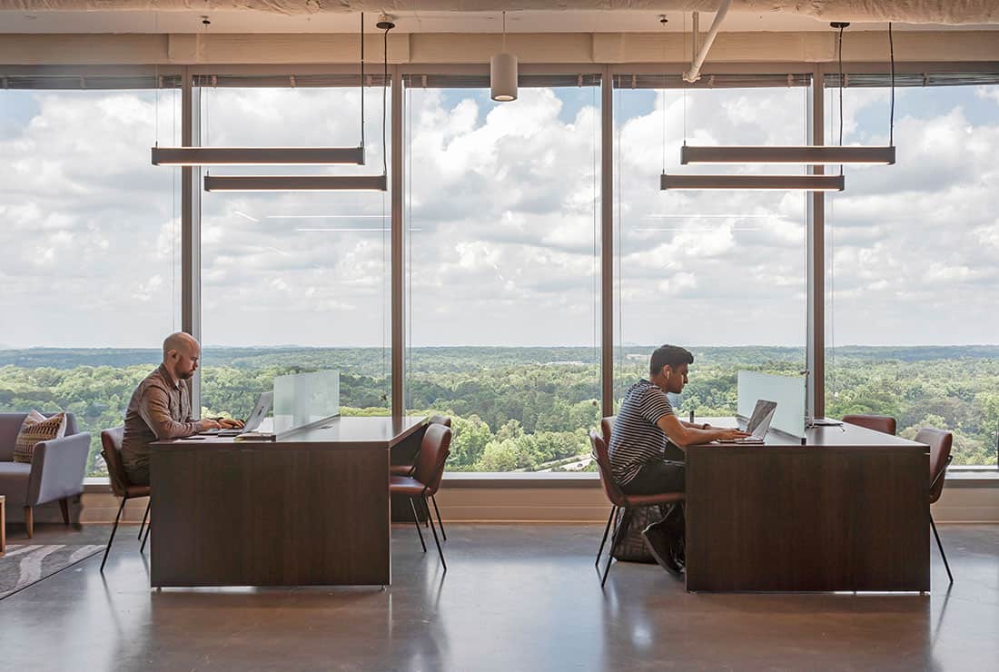 Two members working independently in Coworking area by the window.
