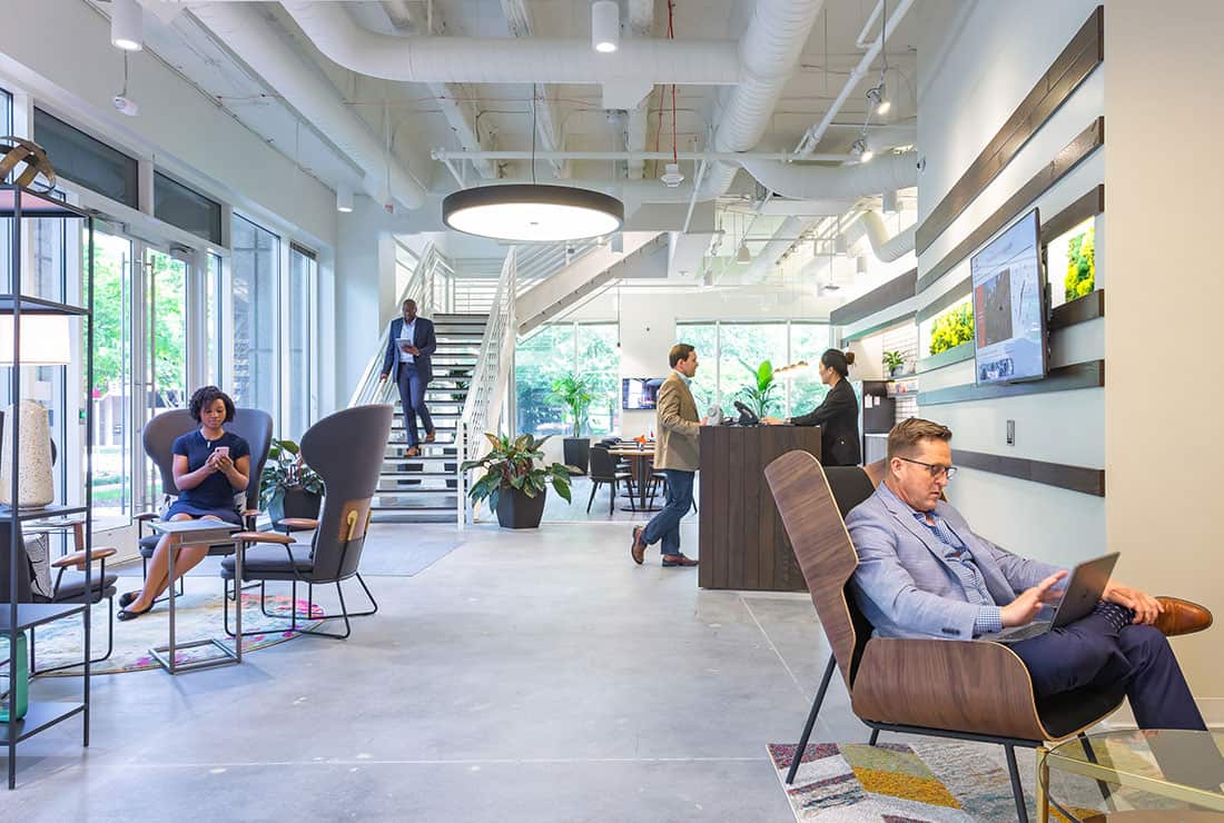 Man talking to the Experience Coordinator at the front desk while members work throughout the Coworking area.