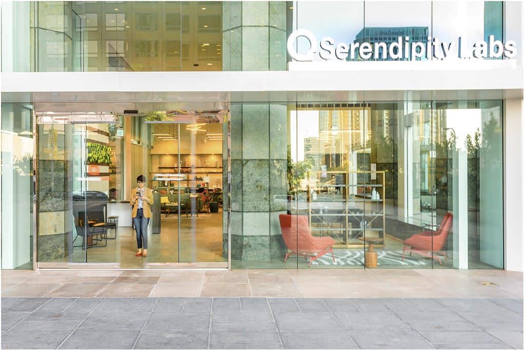 View of the large glass outside entrance to Serendipity Labs with someone standing at the front door. Indoor is visible to passing pedestrians