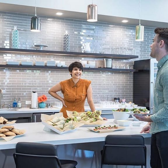 A man and woman talking in the kitchen area in front of catered food.