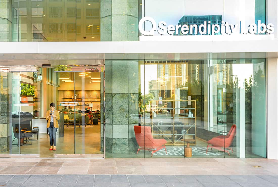 View of the outside entrance to Serendipity Labs with someone standing at the front door. Indoor is visible to passing pedestrians
