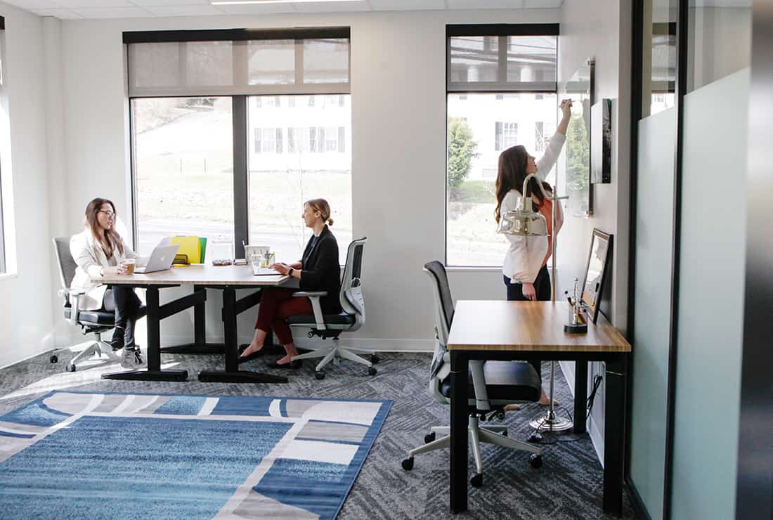 Three women utilizing a three person private office with views of outside and a built-in whiteboard.