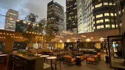 A rooftop patio at dusk features string lights, outdoor sofas, and tables, surrounded by skyscrapers with illuminated windows—perfect for unwinding after a day at Serendipity Labs coworking offices and meeting rooms in the city.